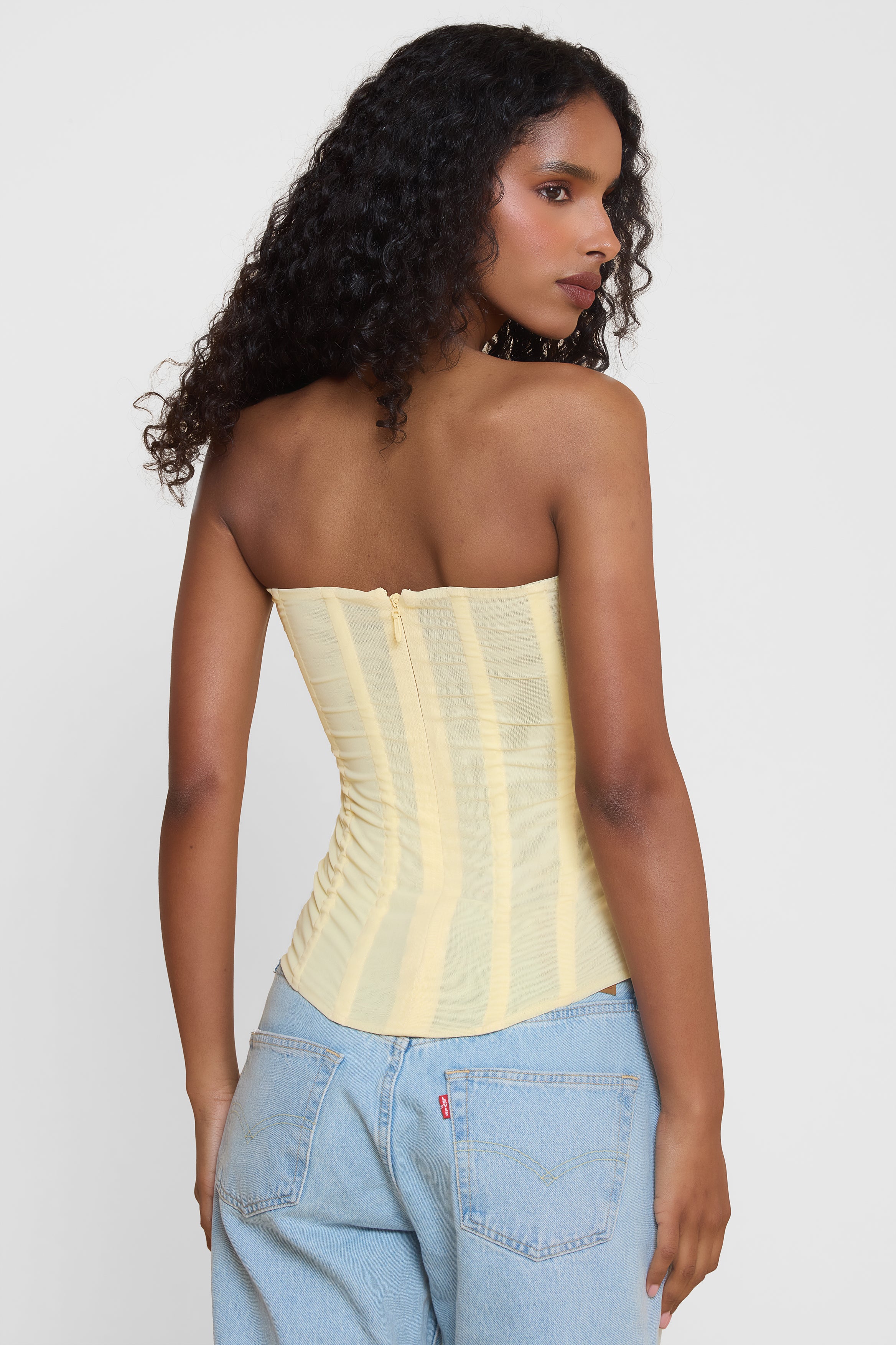 Model wearing Muse Mesh Corset Top in Yellow, back view.