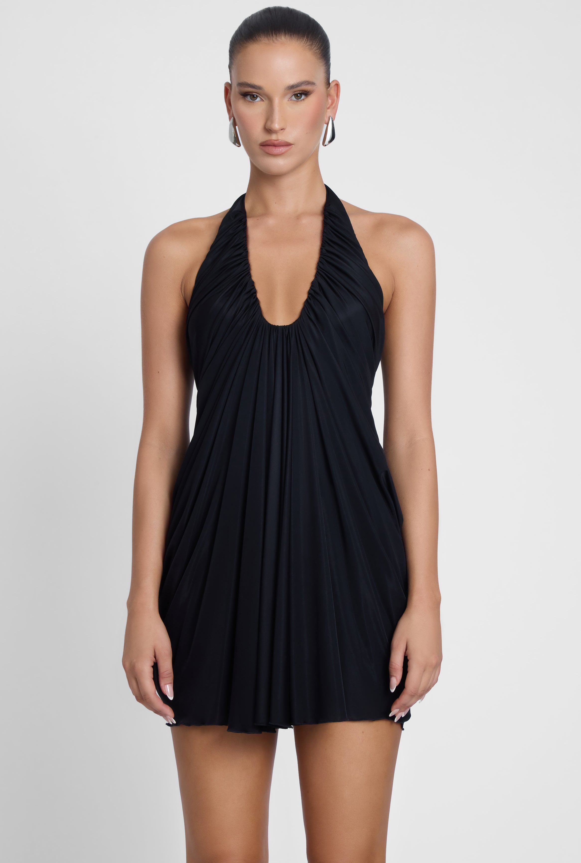 Model is wearing Odyssey Drape Mini Dress Black, front view.